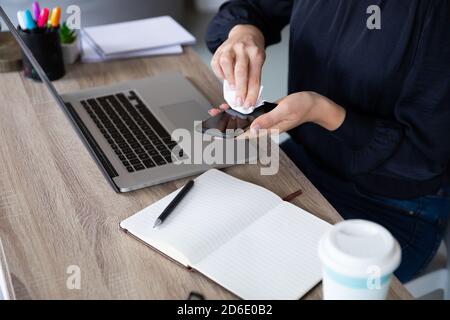Mittelteil einer Frau, die ihr Smartphone mit einem Gewebe abwischt Stockfoto