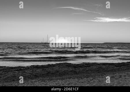 Ein wunderschöner schwarz-weißer Sonnenuntergang an der Küste am unberührten Strand von Es Trenc auf Mallorca. Im Hintergrund des Bildes, einige Segelboote ancho. Stockfoto