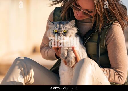 Stilvolle Dame mit ihrer reinrassigen Katze sitzt draußen auf dem Sonnenuntergang. Haustier mit Eigentümer Stockfoto