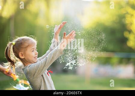 Glückliches 5-jähriges Kind platzt Seifenblasen im Garten. Sommerurlaub in der Natur. Emotionales Porträt von glücklichen und aktiven kleinen schönen Mädchen platzen Stockfoto