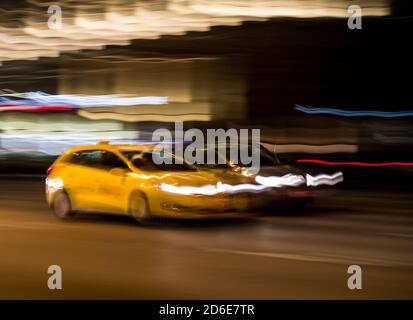Gelbes Taxi auf einer Straße in der Stadt bei Nacht, absichtliche Bewegung verschwimmen Stockfoto