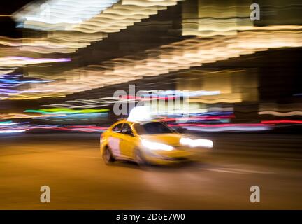 Gelbes Taxi auf einer Straße in der Stadt bei Nacht, absichtliche Bewegung verschwimmen Stockfoto