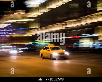 Gelbes Taxi auf einer Straße in der Stadt bei Nacht, absichtliche Bewegung verschwimmen Stockfoto