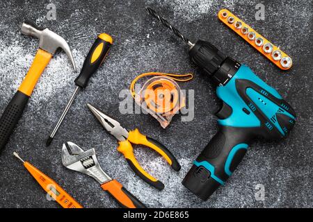 Werkzeugsatz auf dunklem Hintergrund. Sanierungskonzept, Hausarbeit. Flache Lay-Komposition. Elektrobohrer, Schraubendreher, Maßband, Schraubenschlüssel, Messer und h Stockfoto