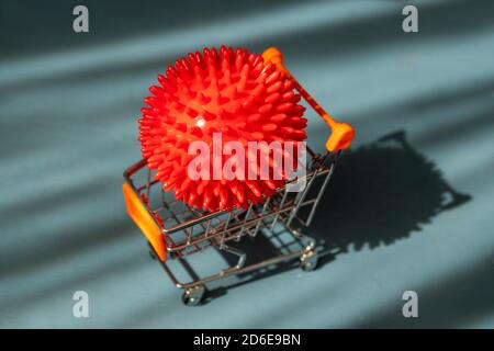 Rote Kunststoff-Corona-Virus-Modell auf Mini-Shopping-Auto-Modell auf blauem Holzhintergrund mit dramatischem Sonnenlicht. Stockfoto