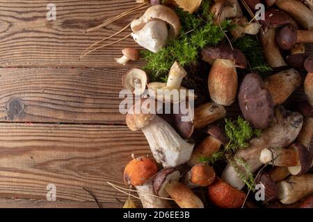 Frische Wildpilze unterschiedlich auf einem hölzernen Hintergrund, Draufsicht, Kopierraum. Herbstkonzept. Stockfoto