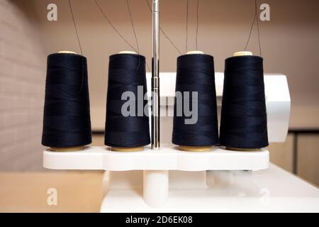 Schwarze Fadenspulen auf moderner Overlock weißer Nähmaschine, professionelle Nähmaschine Stockfoto