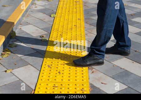 Mann, der auf gelben Blöcken des taktilen Pflasters für blindes Handicap geht.Braille-Blöcke, taktile Fliesen für Sehbehinderte, Tenji-Blöcke.Textured Stockfoto