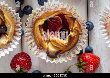 Tartlet mit Erdbeeren, Äpfeln, Heidelbeeren und Zimt auf Holzgrund. Frisches und gebackenes Obst. Stockfoto