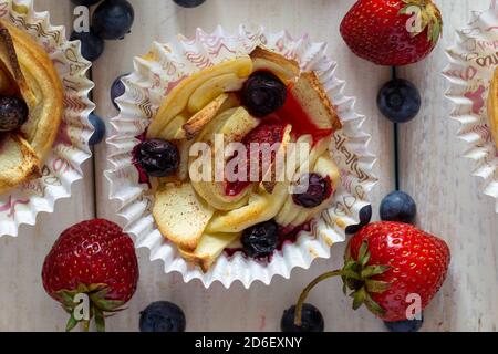 Tartlet mit Erdbeeren, Äpfeln, Heidelbeeren und Zimt auf Holzgrund. Frisches und gebackenes Obst. Stockfoto