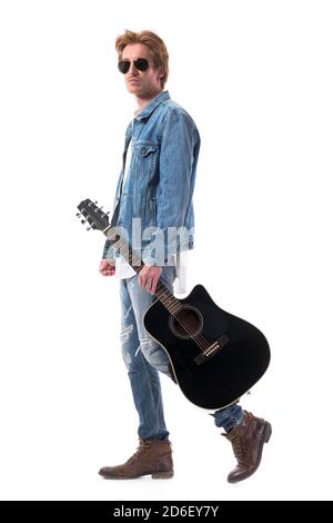 Cool Macho Rocker männlich in Jeans gehen und halten akustische Gitarre tragen Sonnenbrille. Ganzkörper isoliert auf weißem Hintergrund. Stockfoto