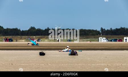 Frau mit Bikini und Sonnenhut liegt im Sand und Sonnenbaden, St. Peter Ording, Strandurlaub Stockfoto