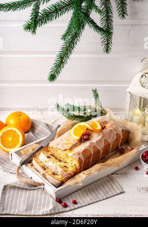 Weihnachtliche Orangenkuchen mit Preiselbeeren und Zuckerzuckerguss auf rustikalem Holzhintergrund. Feiertagsdekoration mit Festoon, Kerzenlaterne und Tannenzweigen. Stockfoto