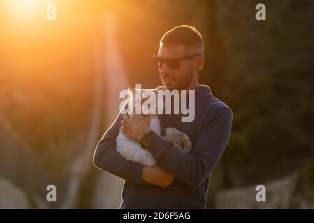 Mann hält seine schöne gepflegte reinrassige Katze draußen auf den Sonnenuntergang. Haustier mit Eigentümer Stockfoto