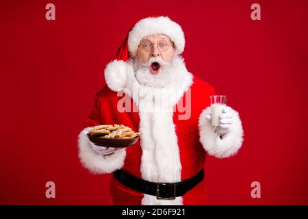 Foto von stauned verrückt santa claus halten x-Mas Frühstück Ingwer Brot Kekse Teller Milchglas tragen rote Kostüm isoliert über Helle Glanzfarbe Stockfoto