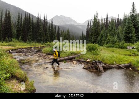 Seitenansicht des Mannes, der in den Bergen wanderte und den Fluss überquerte An bewölktem Tag in British Columbia Stockfoto