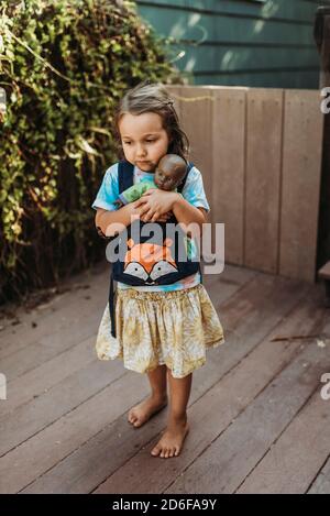 Kleines Mädchen trägt Babydoll in Babytrage draußen im Hof Stockfoto