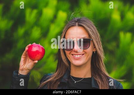 Lächelnde vegane Frau zeigt roten leckeren Apfel auf grünem Hintergrund. Stockfoto