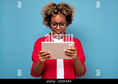 Junge afrikanische lockige Frau schockiert von Nachrichten auf einem digitalen Tablet angezeigt. Stockfoto