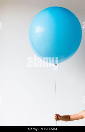 Ernte des Kinderarms, der einen großen blauen Ballon an der weißen Wand hält. Stockfoto