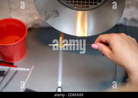 Der Künstler erhitzt das Glas mit einem Gasbrenner. Der Prozess der Herstellung von Glasschmuck. Die Hände des Meisters aus der Nähe Stockfoto