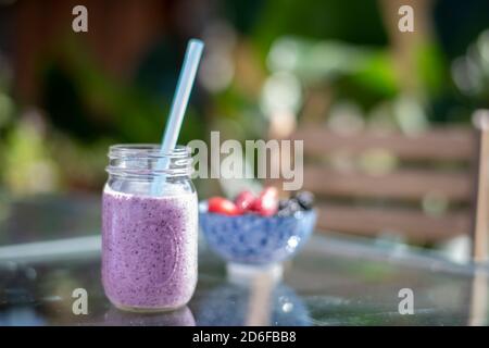 Hausgemachter Beerenmoothie im Einmachglas mit blauem Stroh Außentisch Stockfoto