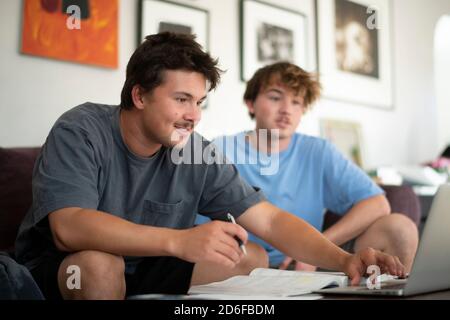 2 junge Erwachsene Männer lächeln und machen Hausaufgaben im Haus Einstellung Stockfoto