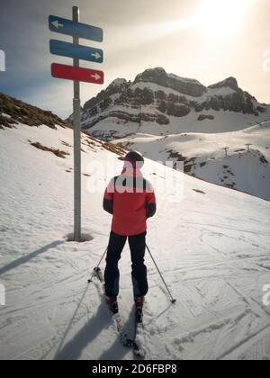 Skifahrer vor einem Skigebiet Wegweiser Zweifel, welche Skipiste zu gehen. Skikonzept Stockfoto