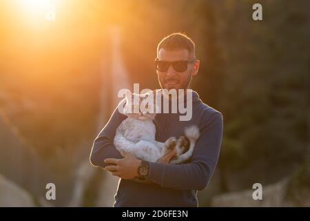 Mann hält in den Händen seine schöne reinrassige Katze draußen auf den Sonnenuntergang. Haustier mit Eigentümer Stockfoto