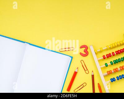 Zurück zur Schule, Bildungskonzept. Weißes Notizbuch mit Schulwerkzeugen, Büroklammern, Zahlen, Bleistiften, Kugelschreiber und Taschenrechner isoliert auf gelbem studi Stockfoto