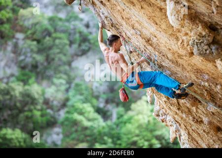 Felskletterer an überhängender Wand. Klettern auf natürlichen Klippen. Starker junger Mann, der sich bemüht, kleine Handgriffe auf anspruchsvoller Strecke zu greifen. Stockfoto