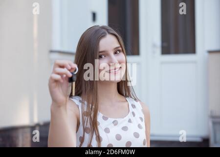 Schöne junge Frau lächelnd und Blick auf die Kamera während des Stehens Auf der Stadtstraße und vorführen der Schlüssel Stockfoto