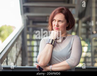 Unzufriedene ältere weibliche Stützkopf mit Faust und wegschauen Es steht außerhalb des modernen Gebäudes Stockfoto