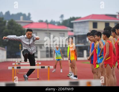 (201017) -- PEKING, 17. Oktober 2020 (Xinhua) -- Luo Laijin (1. L) demonstriert Hürde, während seine Schüler während eines Schuluntergangs im Kreis Luxi, ostchinesische Provinz Jiangxi, am 15. Oktober 2020, darauf blicken. Die 58-jährige Luo Laijin der Mittelschule der Stadt Yinhe im Kreis Luxi arbeitet seit 1982 als P.E.-Lehrer. Obwohl er sich dem Ruhestand nähert, ändert sich sein Eifer und seine Metikulosität für die Leichtathletik-Ausbildung nie. Unter seiner Anleitung haben seine Schüler im Laufe der Jahre insgesamt 1,600 Auszeichnungen in Sportveranstaltungen verschiedener Ebenen gewonnen, und rund 180 Studenten mit Leichtathletik-Special Stockfoto