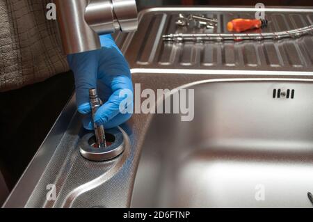 Installation des Wasserhahns an einem Waschbecken. Hände halten eine Küchenarmatur mit elastischen Schläuchen. Reparatur eines Wasserhahns. Stockfoto