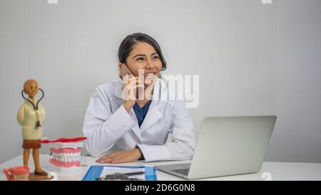 Junge hispanische Dentaltherapeutin, die in ihr am Telefon spricht Büro Stockfoto