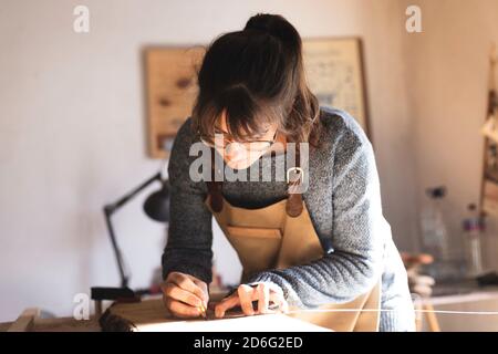 Eine junge Tischlerin, die während der Arbeit mit Holz in einer Schreinerei ein Stück Holz zeichnet. Junge Mädchen Holzarbeiter Gestaltung ein neues Stück Stockfoto