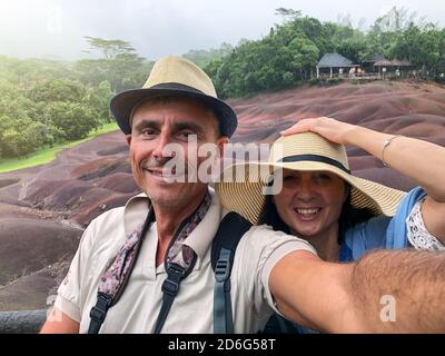 Glückliches Paar mit Hüten und lächelnd auf einem tropischen Inselausflug mit Regen. Stockfoto