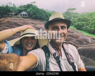 Glückliches Paar mit Hüten und lächelnd auf einem tropischen Inselausflug mit Regen. Stockfoto