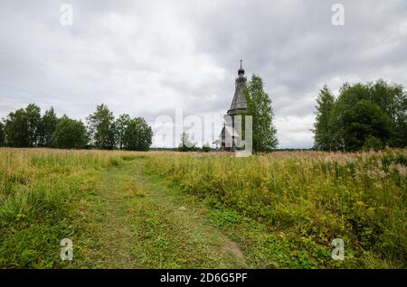 August 2020 - Red Lag. Verlassene hohe Holzkirche in der Mitte eines großen Feldes. Russland, Archangelsk Region Stockfoto