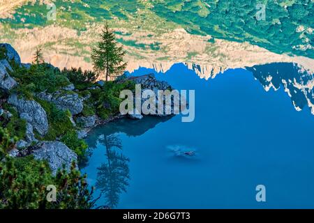 Blick auf den türkisfarbenen See Lago di Sorapiss, Felsformationen und Bäume, die sich im Wasser spiegeln, bei Sonnenaufgang. Stockfoto