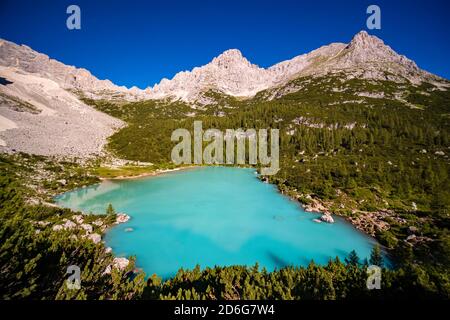 Panoramablick auf den türkisfarbenen See Lago di Sorapiss, den Gipfel des Berges Cima del Laudo in der Ferne, bei Sonnenaufgang. Stockfoto