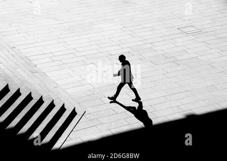 Belgrad, Serbien - 09. Oktober 2020: Schattensilhouette eines Mannes, der Papiere hält, während er auf dem Bürgersteig des Stadtplatzes zur Treppe eines öffentlichen Gebäudes geht, Stockfoto