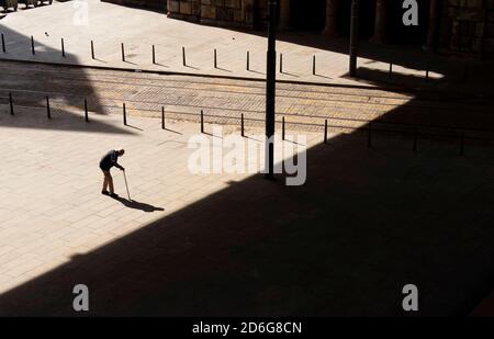 Belgrad, Serbien - 09. Oktober 2020: Silhouette eines alten Mannes, der langsam mit einem Stock über den Stadtplatz in Richtung dunkler Schatten geht, in einem hohen Winkel Stockfoto