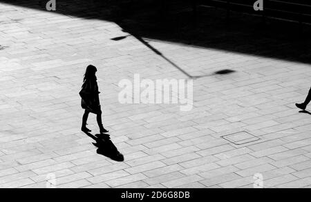 Belgrad, Serbien - 09. Oktober 2020: Schatten Silhouette einer jungen Frau zu Fuß Stadt Platz Bürgersteig, in Hochwinkel-Ansicht schwarz und weiß Stockfoto