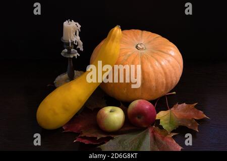 Herbststillleben mit großem Kürbis, Kürbis, Äpfeln und erloschter Kerze in Bronze Kerzenständer auf den fallenden Ahornblättern Stockfoto