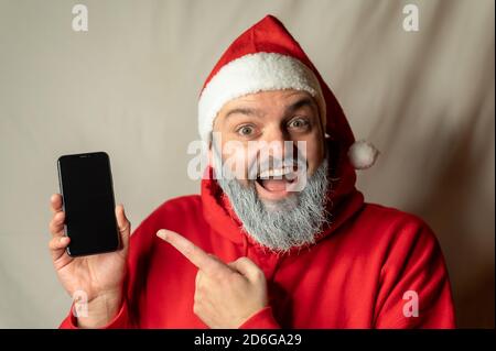 Der Weihnachtsmann zeigt mit dem Finger auf ein Handy und ist begeistert. Stockfoto