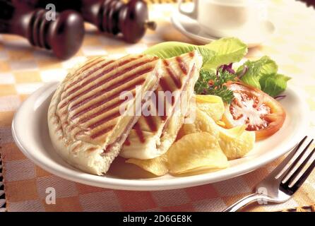 Gegrillter und gepresster Toast mit geräuchertem Schinken, Käse, Kartoffelchips und Salat Stockfoto