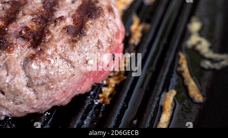 Hamburger Patty wird in einer gusseisernen Grillpfanne gekocht. Verkohlte Brandflecken aus der Pfanne sind deutlich sichtbar. Stockfoto