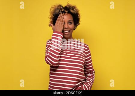 Junge afrikanische Frau schließt ein Auge mit lächelnder Hand Während des optischen Tests Stockfoto